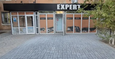 EXPERT-ке көшеден кіреберіс: шыны есіктің үстінде ақ EXPERT әріптері бар қара күнқағар